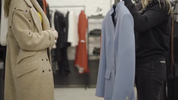 Vue latérale d'une femme caucasienne méconnaissable choisissant des vêtements élégants sur le cintre. Assistante de magasin aidant le client à prendre une décision. Un client riche achetant une tenue dans un centre commercial. Service et achats. — Video