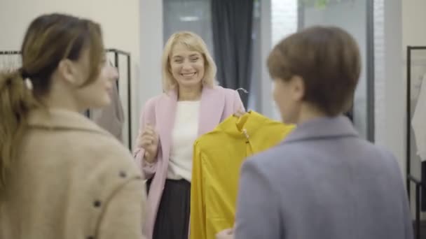 쇼핑몰 친구들에게 노란색 블라우스를 보여 주고 탈의실에 나가는 행복 한 여성. 검은 금요일에 옷을 사고 있는 자신감 있고 아름다운 백인 백인 백인 쇼핑객의 사진. — 비디오