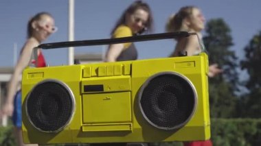 Arka planda disko müziği eşliğinde dans eden 80 'lerin bulanık kadınları ile güneş ışığında sarı antika kayıt cihazının yakın çekimi. Dışarıda antrenman yapan kaygısız beyaz kadın sporcular..