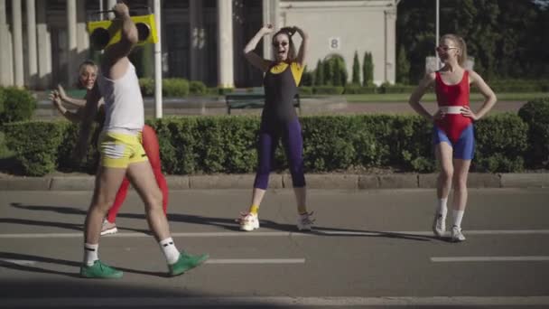 Широкий знімок кокетки 1980-х спортсменів, що прогріваються на сонячній літній вулиці як інструктор фітнесу, що приходить з жовтим магнітофоном. Щасливий чоловік і жінки тренуються на відкритому повітрі. Ретро стиль життя . — стокове відео