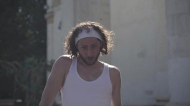 Yakışıklı genç sporcu dışarıda güneş ışığında hızlı yürüyormuş. Gülümsüyor ve kameraya göz kırpıyor. Sportif beyaz adam dışarıda antrenman yapıyor ve gidiyor. Spor ve spor konsepti.