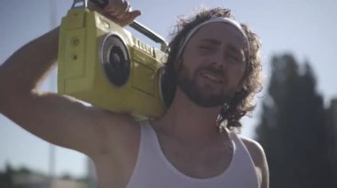 Kaygısız yakışıklı 1980 'lerin erkek portresi dans eden ve disko müziği eşliğinde şarkı söyleyen omzunda retro sarı teyp tutan. Genç beyaz adam gün ışığında dışarıda eğleniyor..