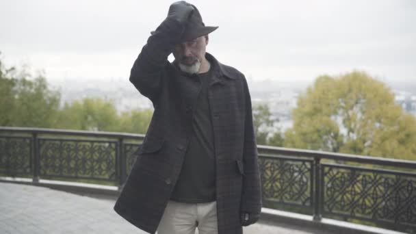 Beau agent secret caucasien portant un chapeau élégant et regardant la caméra. Portrait d'un détective privé professionnel confiant posant à l'extérieur par temps nuageux. Concept d'investigation.