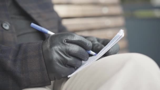 Gros plan de la main masculine en cuir écriture gant avec stylo dans le carnet. Agent de renseignement méconnaissable ou détective privé planifiant une enquête à l'extérieur le jour couvert du printemps ou de l'automne. — Video