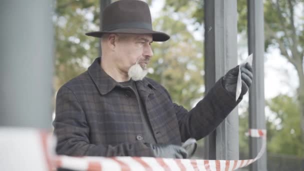 Sidovy av koncentrerad detektiv eller spion tittar genom förstoringsglas på paketet med piller, och tänker. Porträtt av självsäker elegant professionell vit man som utreder brott utomhus. — Stockvideo