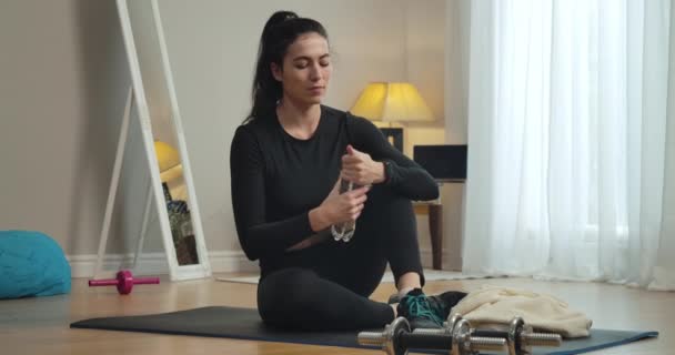 Ευρεία βολή του λεπτού αυτοπεποίθηση γυναίκα άνοιγμα μπουκάλι και πίνοντας δροσιστικό νερό μετά την εκπαίδευση στο σπίτι. Πορτρέτο νεαρής Καυκάσιας αθλήτριας σε εσωτερικούς χώρους. Κινηματογράφος 4k ProRes HQ. — Αρχείο Βίντεο