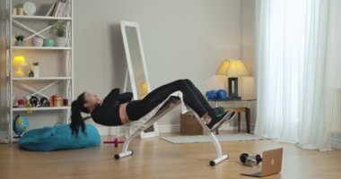 Kendine güvenen sporcunun evdeki egzersiz tezgahında basın pompalaması geniş açılı bir bakış açısı. İnce, güzel, esmer, beyaz kadın portresi içeride çalışıyor. Sinema 4k ProRes Merkezi.