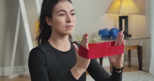 Camera moves down along slim body of young concentrated sportswoman training hands with resistance band. Young beautiful Caucasian woman training at home. Cinema 4k ProRes HQ. — Stock Video