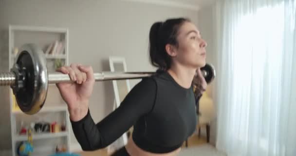 Live camera follows fit sportswoman squatting with barbell on shoulders. Focused young slim Caucasian sportswoman training at home. Sport and workout concept. Cinema 4k ProRes HQ. — Stock Video