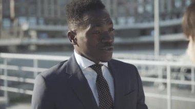 Kendine güvenen Afro-Amerikan iş adamının beyaz iş kadınıyla açık havada konuşmasının yakın plan portresi. Genç yakışıklı adam günışığında kadınlarla projeyi tartışıyor. İşbirliği ve iş.