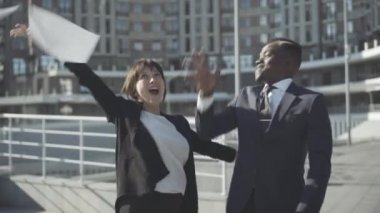 Çok ırklı ortaklar belgeleri kusuyor ve gün ışığında sarılıyorlar. Mutlu beyaz kadın ve Afrikalı Amerikalı erkeğin portresi iş bölgesinde başarıya seviniyor. Zenginlik ve takım çalışması kavramı.