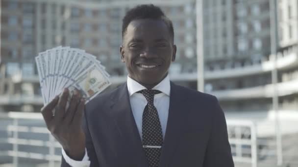 Empresário afro-americano sorrindo mostrando dinheiro e polegar para a câmera. Retrato de empreendedor de sucesso confiante ou CEO posando com dólares na luz do sol ao ar livre. Conceito de riqueza e sucesso. — Vídeo de Stock