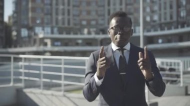 Gözlüklü neşeli Afro-Amerikan iş adamı kameraya bakıyor ve açık havada dans ediyor. İş bölgesinde eğlenen genç bir adamın portresi. Başarı ve neşe kavramı.