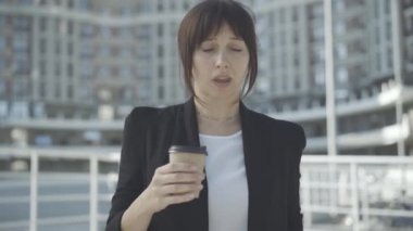 Gün ışığında esneyen ve kahve içen yorgun genç iş kadınının portresi. Yorgun, beyaz bir kadın iş bölgesinde sıcak içecekle ayakta duruyor. Aşırı çalışma kavramı.