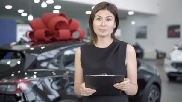 Portret van zelfverzekerde autodealer met documenten die in de showroom praten. Jonge mooie blanke vrouw die auto 's verkoopt in de dealer. Auto-industrie en beroep. — Stockvideo