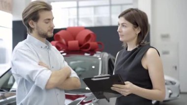 Profesyonel araba satıcısı müşterisiyle galeride konuşuyor. Kendine güvenen beyaz kadın ve adamın galeride araç alımını tartışan portresi. Alım ve satım kavramı.