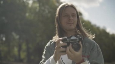 Açık havada fotoğraf çeken genç ve mutlu hippi adamın yakın plan portresi. Neşeli, içine kapanık beyaz adam güneşli yaz gününün tadını çıkarıyor. Hobiler ve 1960 'ların yaşam tarzı konsepti.