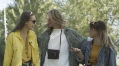 Neşeli hippi adam neşeli kadınlara sarılıyor ve kameraya gülümsüyor. Güneşli yaz gününde güneş gözlüklü üç pozitif retro insanın dışarıda poz verişi. 1960 'ların yaşam tarzı ve pasifizmi.