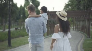 Yaz parkında gezen mutlu, ırklar arası aile manzarası. Kafkasyalı bir baba, Orta Doğulu bir anne ve güneşli bir günde gezip konuşan melez bir oğul. Birlik kavramı.