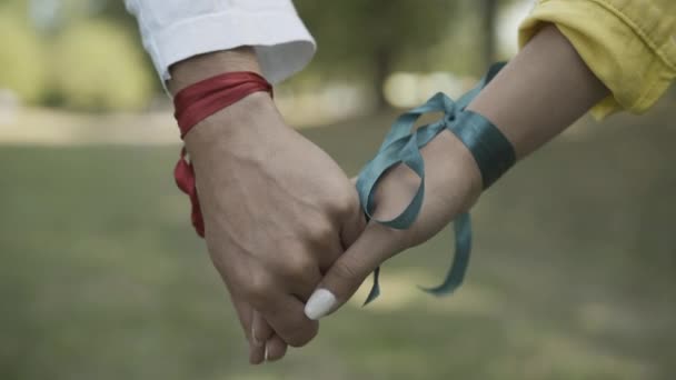 Close-up of male and female Caucasian hands with ribbons in sunlight. Unrecognizable hippie man and woman holding hands outdoors. Pacifism and 1960s lifestyle. — Stock Video