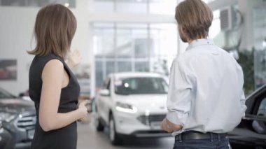 Genç beyaz erkek ve kadının galeride yeni lüks arabalara bakması ve konuşması. Profesyonel satıcı ve başarılı alıcı galeride araçları tartışıyor. Otomatik iş kavramı.