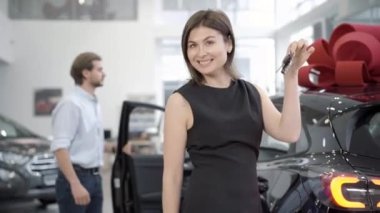 Arka planda araç kapısını açan bulanık genç adam pozu veren neşeli, güzel bir kadın. Galeride genç, beyaz bir alıcı var. Eğlence ve otomobil endüstrisi.