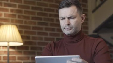 Kendine güvenen esmer iş adamının tablet kullanan, gözlerini ovuşturan ve düşünen yakın plan portresi. Hafta sonları evde çalışan yorgun beyaz bir adam. İş stresi ve aşırı çalışma kavramı.