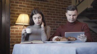 Tablette internette sörf yapan yakışıklı bir adam. Evde kahvaltıda kitap okuyan bir kadın gibi. Zengin, beyaz bir çift sabahları evde kahve içiyor. Ev hayatı kavramı.