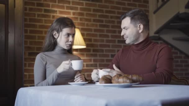 有自信的夫妇，有年龄差异的小杯，喝咖啡或茶，并在镜头前微笑。白人男子和妇女在室内早餐时在豪华房子里摆姿势的画像. — 图库视频影像
