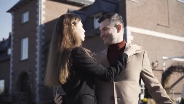 Ricca coppia caucasica con differenza di età in posa all'aperto nella giornata di sole con lussuosa casa sullo sfondo. Felice giovane bella donna baciare l'uomo sulla guancia e sorridente alla macchina fotografica. — Video Stock