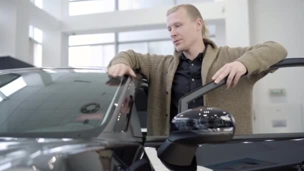 Portret van een blanke man die bij een zwarte auto staat met een open deur en glimlacht naar de camera. Succesvol vertrouwen koper kiezen voertuig in showroom of dealerovereenkomst. Automobielindustrie en bedrijfsleven. — Stockvideo