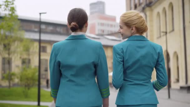Camera follows two confident stewardesses strolling in European city and talking. Back view of slim young Caucasian women walking and chatting during travelling. Tourism and occupation. — Stock Video