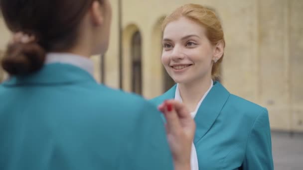 Portrait of young beautiful woman in stewardess uniform talking with coworker outdoors. Positive smiling Caucasian lady chatting with colleague. Beauty and femininity concept. — Stock Video