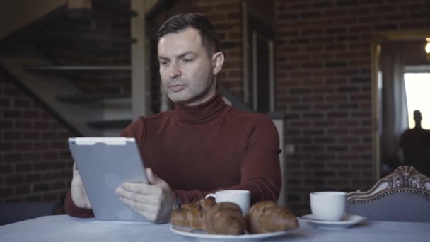 Tablette internette gezen kendine güvenen işadamının portresi. Alt katta yürüyen ve sarılan genç bir kadın olarak. Hafta sonları evde yaş farkı olan mutlu beyaz çift.. — Stok video