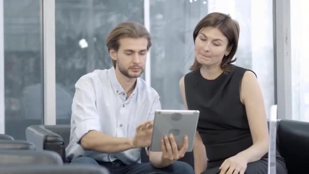 Homme et femme caucasiens concentrés utilisant la tablette et parler. Portrait de collègues ou de partenaires élégants qui discutent d'affaires à l'intérieur. Style de vie et concept d'entreprise. — Video