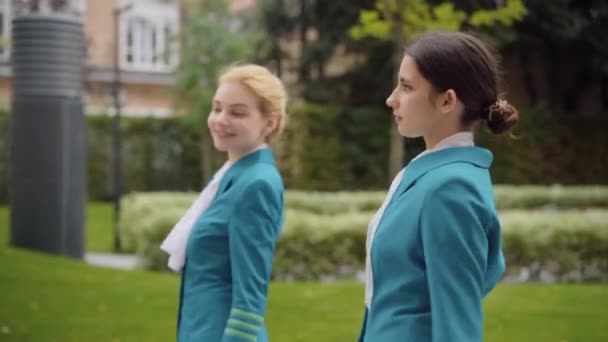 Sidovy av två självsäkra vackra kaukasiska kvinnor promenader i staden. Smala unga eleganta flygvärdinnor strosar utomhus på molnig dag. Begreppet yrken och yrken. — Stockvideo