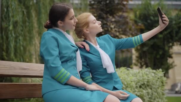 Duas jovens mulheres positivas em uniforme de aeromoça tomando selfie no smartphone. Amigos caucasianos magros confiantes fotografando ao ar livre na rua da cidade. Femininidade e turismo conceito. — Vídeo de Stock