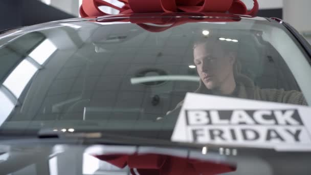 Selbstbewusster Mann sitzt am Black Friday im Neuwagen und begutachtet Auto. Porträt eines erfolgreichen kaukasischen männlichen Käufers, der sich für ein Fahrzeug im Autohaus oder Showroom entscheidet. — Stockvideo