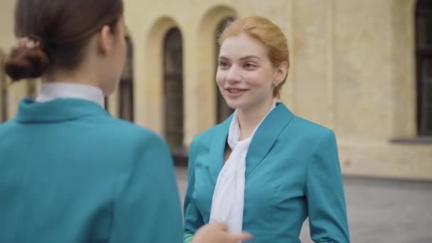 Portrét mladé usměvavé ženy mávající kolegyni na rozloučenou a odcházející. Šťastná elegantní kavkazská letuška opouštějící přítele nebo spolupracovníka na městské ulici. Cestovní ruch a přátelství. — Stock video