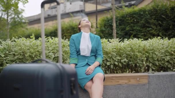 Wide shot of confident young stewardess smoking outdoors with luggage standing at front. Beautiful Caucasian lady resting on break. Lifestyle and professions concept. — Stock Video