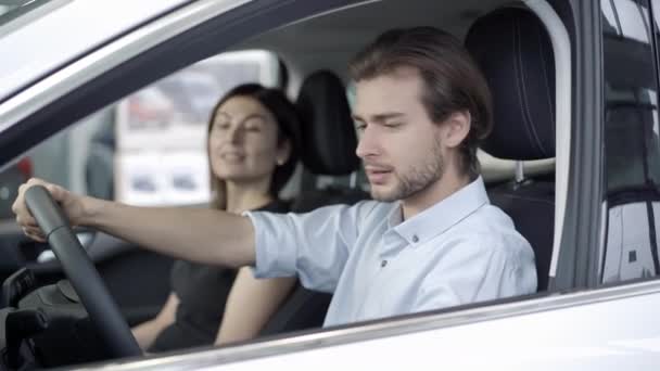 Pohled z boku portrét pohledného mladého muže sedícího v autě se ženou a mluvícího. Úspěšný pár vybírá nové vozidlo v prodejně nebo showroomu. Koncept bohatství a úspěchu. — Stock video