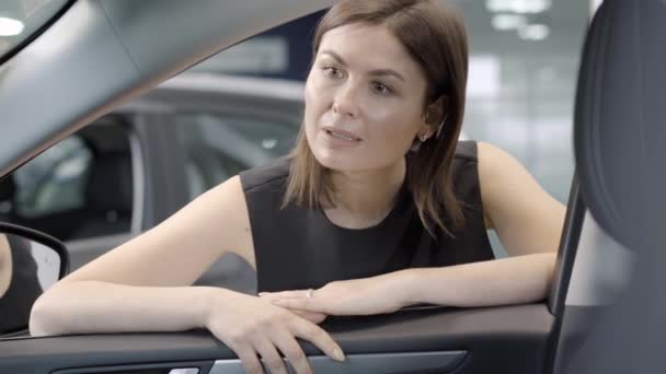 Портрет молодой успешной женщины, смотрящей в машину и думающей. Уверенная в себе элегантная кавказская деловая женщина выбирает новый автомобиль в автосалоне или салоне. Бизнес и автомобильная промышленность. — стоковое видео