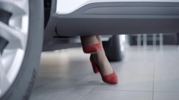 Mujer caucásica elegante irreconocible sentado en el asiento de los conductores levantando los pies y cerrando la puerta del coche. Exitosa mujer de negocios en tacones rojos sentada en automóvil. Industria automotriz y concepto empresarial. — Vídeos de Stock