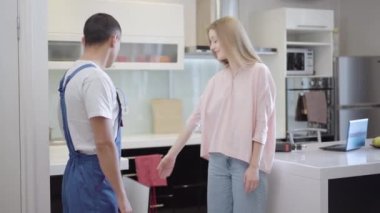 Genç ve güzel bir kadın servis elemanıyla kırık mutfak dolabını tamir etmeyi tartışıyor. Onarım hizmetlerinden yararlanan beyaz bir apartman sahibinin portresi. Marangoz kırıkları onarıyor..