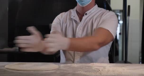 Chef masculino irreconocible en máscara facial Covid aplaudiendo con guantes sobre masa de pizza. Cocinero profesional caucásico cocina sabrosa plato italiano en la cocina del restaurante en el interior. Sede del cine 4k ProRes. — Vídeo de stock