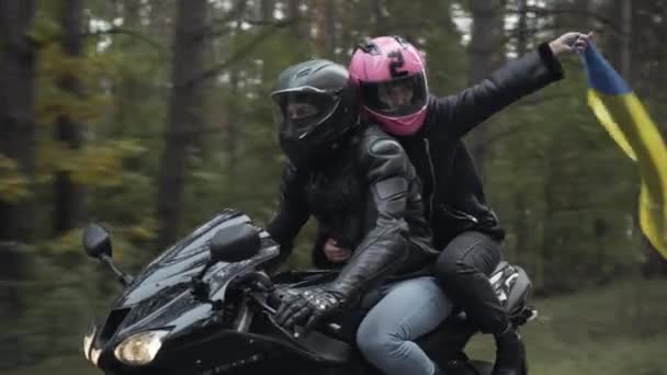 Young interracial couple in helmets riding motorbike with woman holding Ukrainian flag. Middle Eastern man and Caucasian woman racing with national symbol. Pride and lifestyle concept. — Stock Video