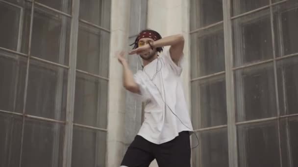 Портрет молодого хіпі-виконавця танцює в міському будинку на вулиці. Радісний кавказький чоловік з дредами, що рухаються руками і посміхаються перед камерою. Хлопець у сонцезахисних окулярах.. — стокове відео