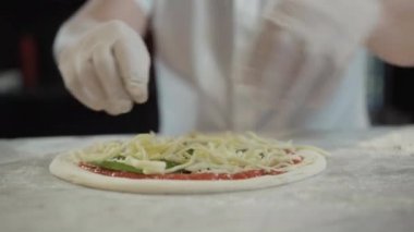 Mutfaktaki çiğ pizzaya peynir ekleyen tanınmayan aşçıya yakın çekim. Restoranda ya da pizzacıda İtalyan yemeği pişiren beyaz bir aşçı. Mutfak konsepti.