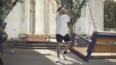 Açık havada güneş gözlüklü, kendinden emin, gülümseyen genç adamın geniş çekim dansı. Şehirde güneşli bir günde dans eden beyaz erkek break dansçı portresi..