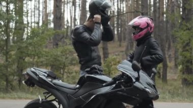 Kendine güvenen motorcunun kask takması ve sevgilisinin onu bağlaması. Bulutlu bulutlu açık havada hızlı yarışa hazırlanan ırklar arası genç çift..